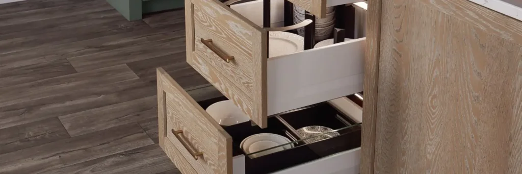 Open wooden kitchen drawers showing organised shelves with plates and bowls inside a cabinet