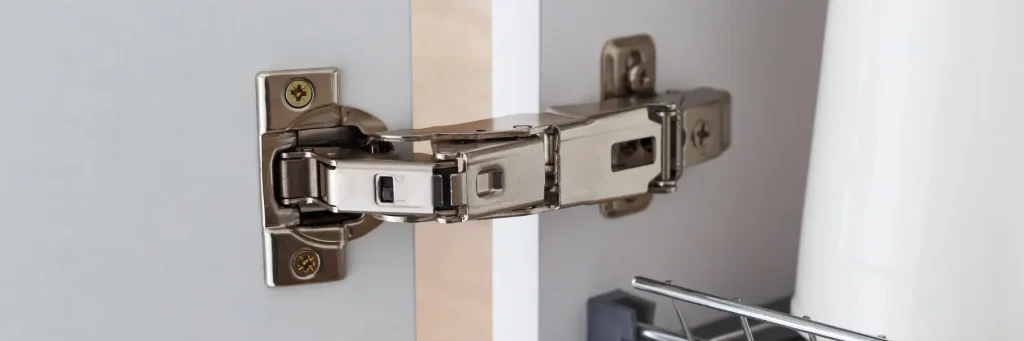 Close-up of a metal concealed cabinet hinge installed on a white wooden door and frame.